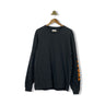 A long sleeve black t-shirt with orange text on the sleeves, displayed on a hanger against a white background.